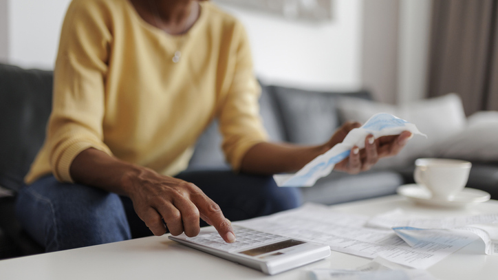 Close up of a mid adult woman checking her energy bills at home, sitting in her living room. She has a worried expression